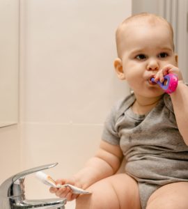 Cute baby sitting by a sink brushing teeth, promoting oral hygiene habits.